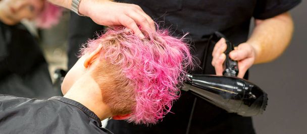 Сушка короткой розовой стрижки кавказки с черным феном руками парикмахера в парикмахерской, крупным планом - Фото, изображение