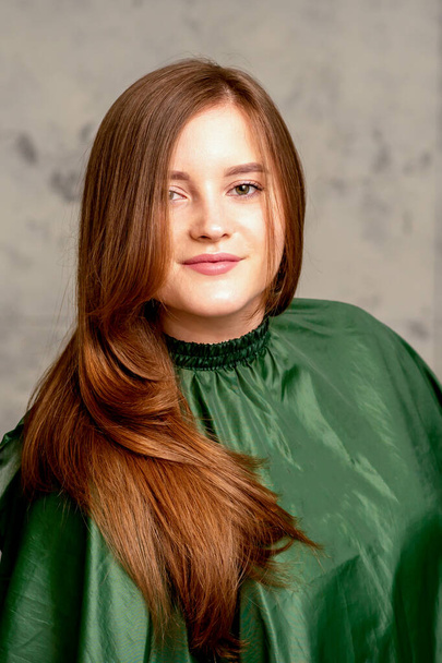 De modieuze jonge vrouw. Portret van het prachtige vrouwelijke model met lang haar en make-up. schoonheid jong Kaukasisch vrouw met een bruin krullend kapsel op de achtergrond van een grijze muur - Foto, afbeelding