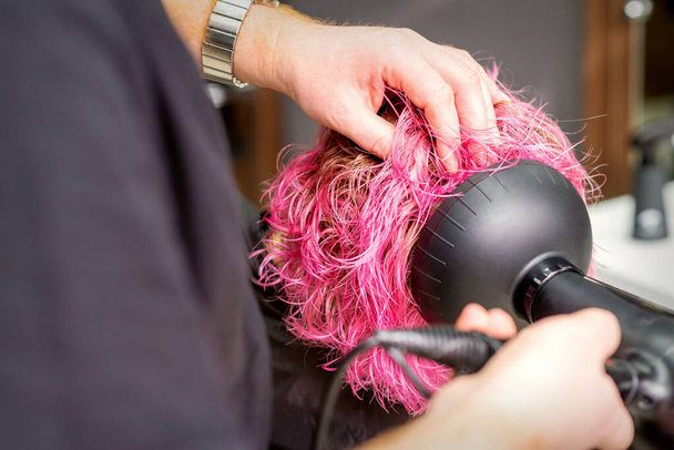 Suszenie krótkie różowe Bob fryzura młodej białej kobiety z czarną suszarką do włosów z pędzlem przez ręce męskiego fryzjera w salonie fryzjerskim, zbliżenie - Zdjęcie, obraz