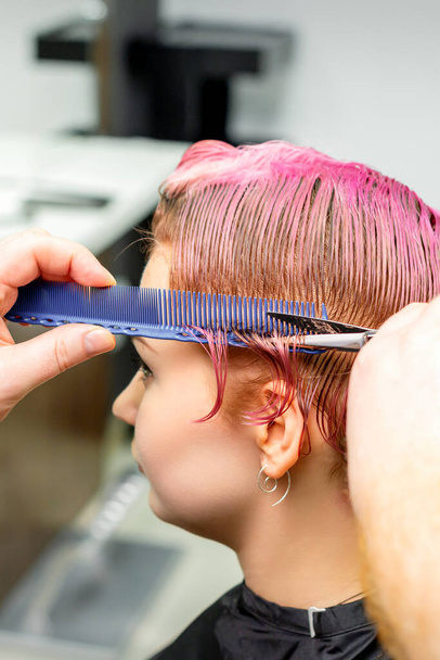 Coupe de cheveux de cheveux roses courts teints mouillés de jeune femme caucasienne par un coiffeur masculin dans un salon de coiffure - Photo, image