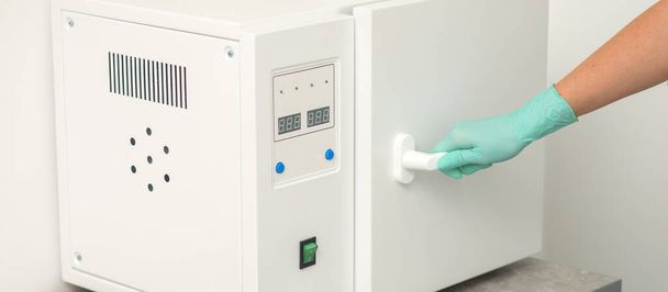 esteticista en guantes de protección cerrar la puerta de la máquina para la desinfección de herramientas antes de los procedimientos médicos - Foto, imagen