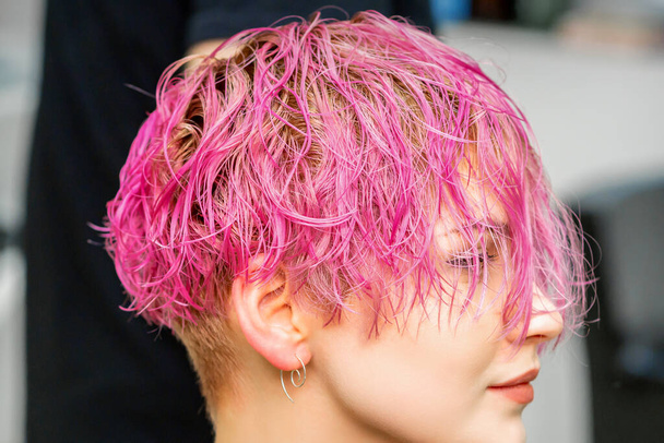 Hermosa joven mujer caucásica que recibe un nuevo peinado corto rosa en el salón de peluquería - Foto, imagen