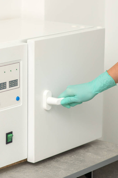 Kosmetyk w rękawiczkach ochronnych zamyka drzwi maszyny do dezynfekcji narzędzi przed zabiegami medycznymi - Zdjęcie, obraz