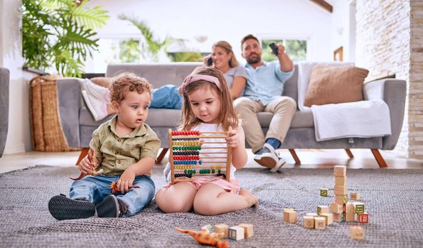 Development, family and children with math toys and playing with building blocks in the house living room. Education, mother and relaxed father watching tv with kids or siblings learning from a game. - Photo, Image
