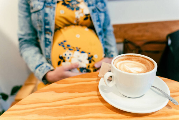 Hamile kadın kahvesini iç. Mutlu hamilelik kızı restoranda sıcak kahve içiyor. Enerji ve tazelik kavramı için kahvaltıyı temsil et - Fotoğraf, Görsel