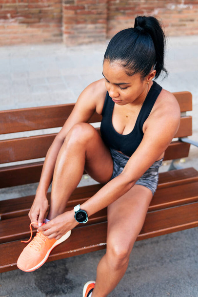 latin sportswoman lacing up her running shoes before her workout, urban sport and healthy lifestyle concept - Фото, зображення