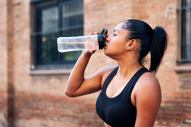 portrait of a sportswoman drinking water during a break in her workout, urban sports and healthy lifestyle concept - Фото, зображення