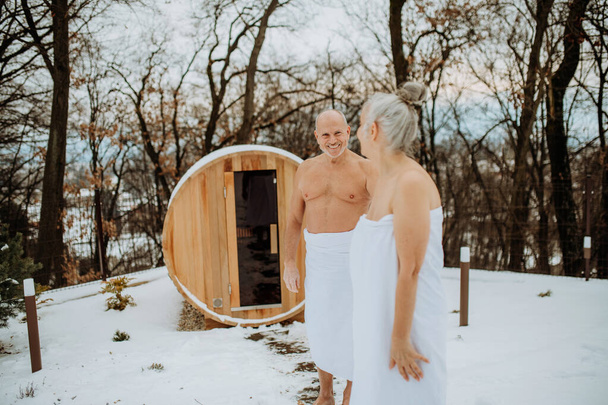 Senior woman in towel with her husband coming out from outdoor sauna during a cold winter day. - Foto, imagen