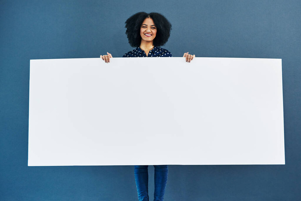 Tengo una gran noticia. Imagen del estudio de una joven mujer sosteniendo un cartel en blanco sobre un fondo azul - Foto, imagen