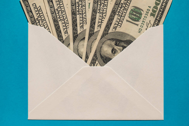 Dollarnoten sparen Geld in einem Umschlag auf blauem Hintergrund. Konsum und Wirtschaft sammeln Geld. Trinkgeld. Unternehmen, Finanzen, Sparen, Banken und Menschen Konzept. Zusätzliches Geld, passiv - Foto, Bild