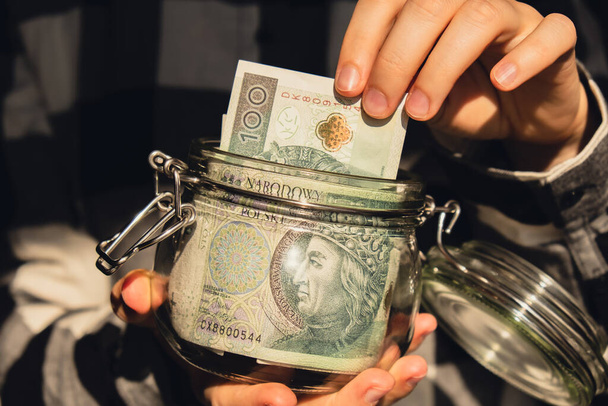 Polish zloty banknote saving money in glass jar. Unrecognizable woman moderate consumption and economy Collecting money. Tips. Business, finance, saving, banking and people concept. Extra money - Photo, image
