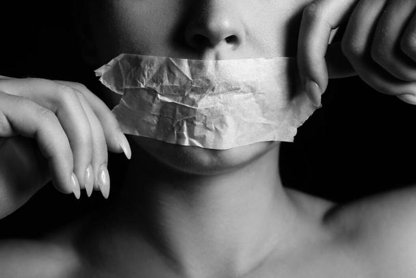 Mujer joven con la boca pegada sobre fondo oscuro, primer plano. Concepto de censura - Foto, Imagen
