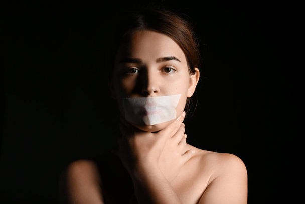 Karanlık arka planda ağzı bantlanmış genç bir kadın. Sansür kavramı - Fotoğraf, Görsel