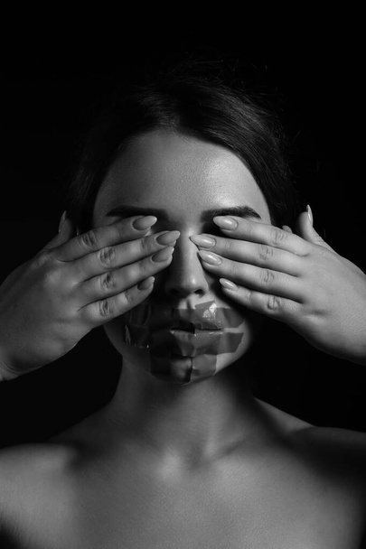 Young woman with taped mouth covering her eyes on dark background. Censorship concept - Photo, Image