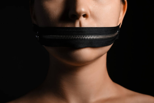 Giovane donna con cerniera sulla bocca sullo sfondo scuro, primo piano. Concetto di censura - Foto, immagini