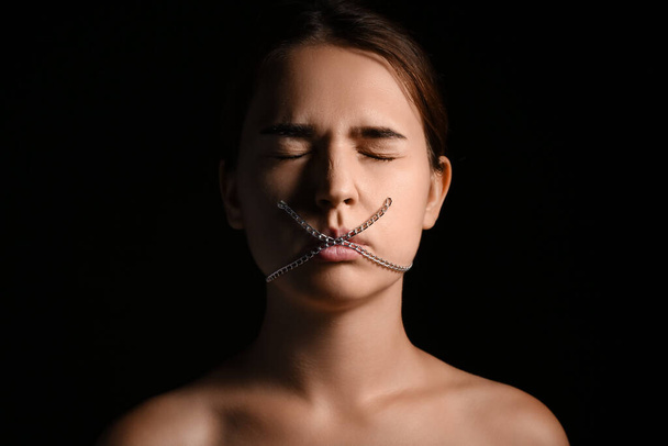 Mladá žena s řetězem na ústech na tmavém pozadí. Koncept cenzury - Fotografie, Obrázek