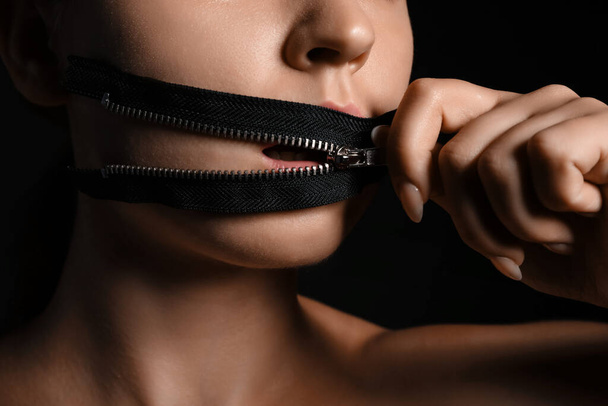 Junge Frau mit Reißverschluss am Mund vor dunklem Hintergrund, Nahaufnahme. Zensurkonzept - Foto, Bild
