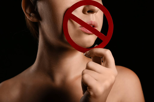 Νεαρή γυναίκα με ταμπέλα ποτοαπαγόρευσης σε σκούρο φόντο. Έννοια λογοκρισίας - Φωτογραφία, εικόνα