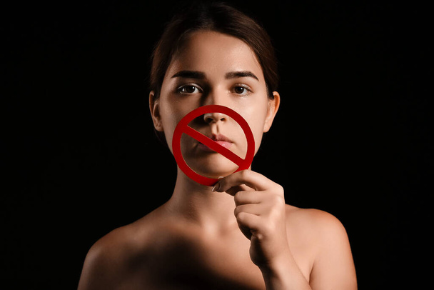 Νεαρή γυναίκα με ταμπέλα ποτοαπαγόρευσης σε σκούρο φόντο. Έννοια λογοκρισίας - Φωτογραφία, εικόνα