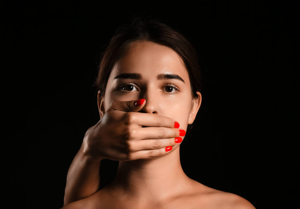 Χέρι που καλύπτει το στόμα της νεαρής γυναίκας σε σκούρο φόντο. Έννοια λογοκρισίας - Φωτογραφία, εικόνα