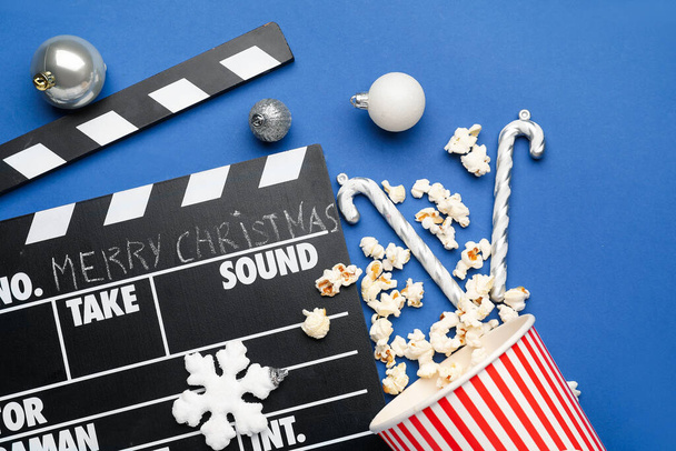 Filmklöppel, Eimer Popcorn und Weihnachtskugeln auf blauem Hintergrund - Foto, Bild