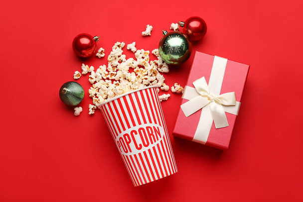 Bucket of popcorn with Christmas balls and gift on red background - Foto, immagini
