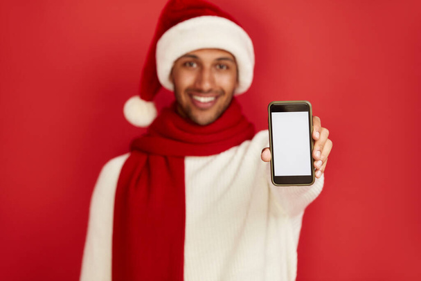 Happy Man Using Smartphone. Multiracial Guy in Santa Hat Smiling while Showing Cellphone, Chatting in Social Media, Enjoying Mobile Service. Empty Copy Space for Advertisement, Indoor Studio Shot  - Foto, immagini