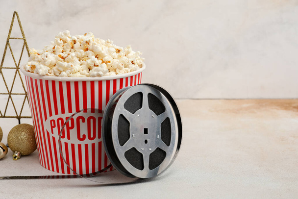 Bucket of popcorn with film reel and Christmas decor on light background - Photo, Image