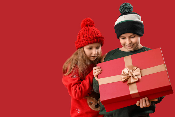 Little children opening Christmas gift on red background - Photo, Image
