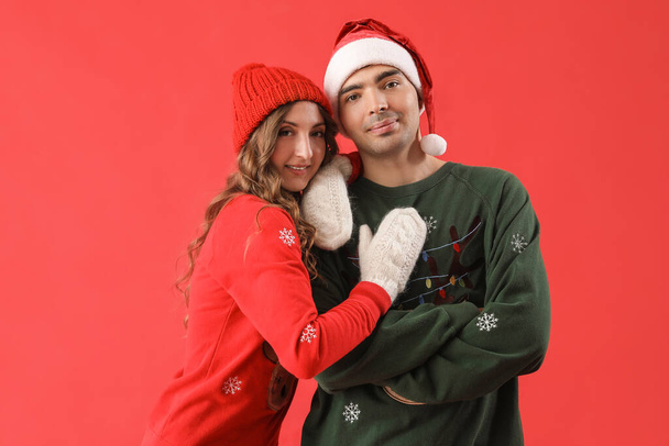 Loving couple in Christmas sweaters on red background - Photo, Image