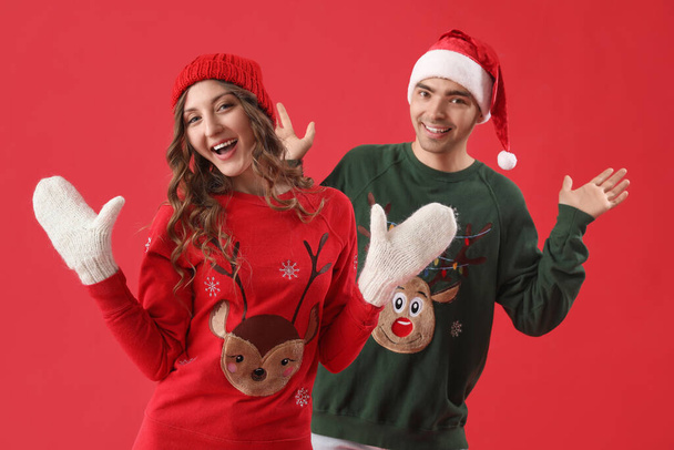 Loving couple in Christmas sweaters on red background - Zdjęcie, obraz