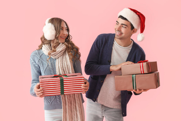 Junges verliebtes Paar mit Weihnachtsgeschenken auf rosa Hintergrund - Foto, Bild