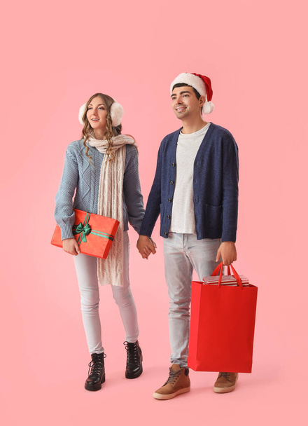 Young couple in love with Christmas gift and shopping bag on pink background - Фото, изображение