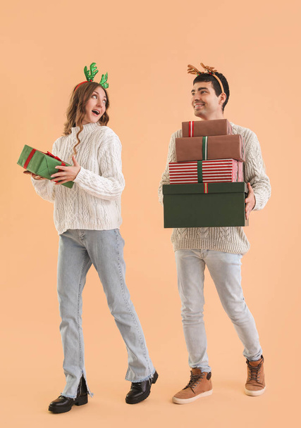Loving couple in reindeer horns with Christmas presents on beige background - Φωτογραφία, εικόνα