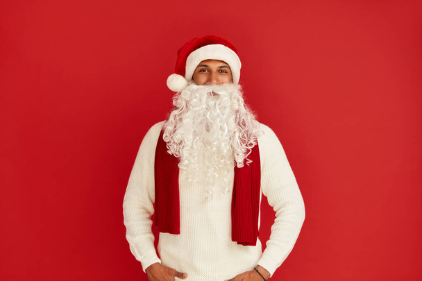 Santa Claus Posing Studio. Portrait of Happy Multiracial Handsome Guy Standing and Smiling. Indoor Studio Shot, Isolated on Red Background  - Photo, Image