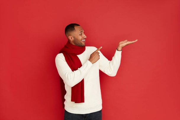 Smiling Man Pointing Hand. Positive Multiracial Guy Pointing Away Paying Your Attention at Empty Space for Advertisement. Indoor Studio Shot Isolated on Red Background  - Foto, Bild