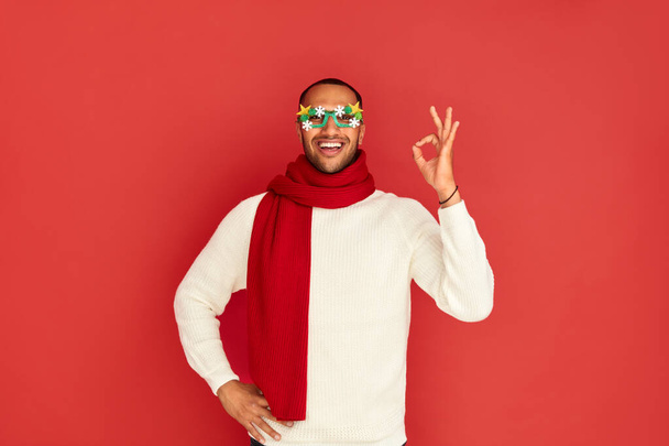 Smiling Man Showing Ok Gesture. Satisfied Multiracial Guy Making Ok Symbol with Fingers, Approving, Satisfied. Indoor Studio Shot Isolated on Red Background  - Photo, Image