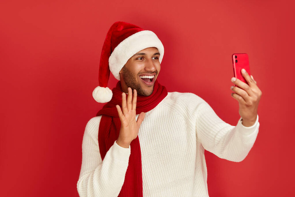 Happy Man käyttää älypuhelinta. Monirotuinen kaveri Santa Hat hymyillen samalla videoiden matkapuhelin, Chattailu sosiaalisessa mediassa, Nautitaan Mobile Service. Tyhjä Kopioi tilaa mainos,  - Valokuva, kuva