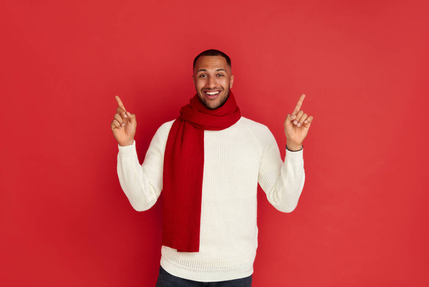 Smiling Man Pointing Hand. Positive Multiracial Guy Pointing Away Paying Your Attention at Empty Space for Advertisement. Indoor Studio Shot Isolated on Red Background  - Zdjęcie, obraz