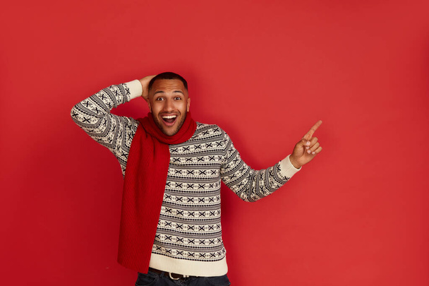 Shocked Man Pointing Aside. Astonished Multiracial Guy in Pointing at Copy Space and Looking With Amazement. Indoor Studio Shot Isolated on Red Background  - Photo, image