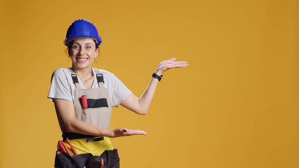 Portrait of construction worker advertising sideways space, pointing left or right to show message in studio. Indicating sides direction to do advertisement. Woman with refurbishment work. - Photo, Image