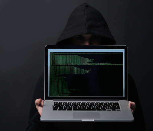 Technology could be your downfall. an unidentifiable computer hacker holding up a laptop against a dark background - Φωτογραφία, εικόνα