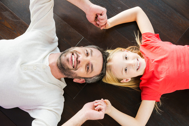 Vader en dochter hand in hand en liggend op de vloer - Foto, afbeelding