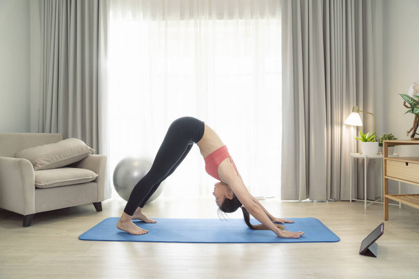 Mujer asiática ejercicio y estiramiento en su dormitorio, su intento de hacer delgado por tomar Yoga, cardio, fitness en casa entre cuarentena - Foto, imagen