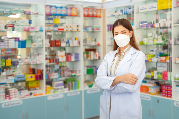 Eczane dükkanında koruma maskesi takan Asyalı bir eczacı kadın müşterisiyle ilaç ve eczane satışı yapıyor. - Fotoğraf, Görsel