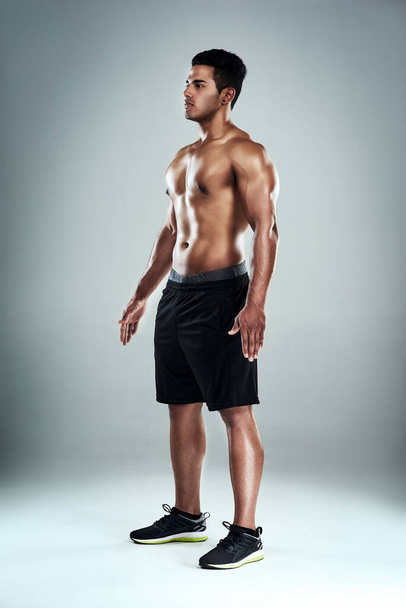 His body has been perfectly sculpted. Full length shot of a sporty young man standing against a grey background - Fotó, kép