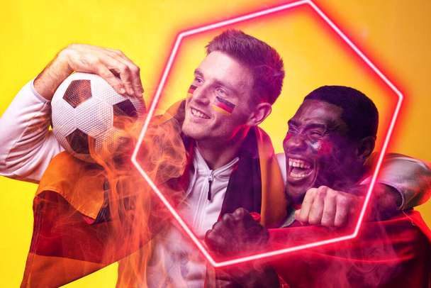 Composite of multiracial cheerful male players with german flag, ball and illuminated hexagon. Sport, soccer, competition, neon, illustration, glowing, smoke, happy, team sport and abstract concept. - Photo, Image