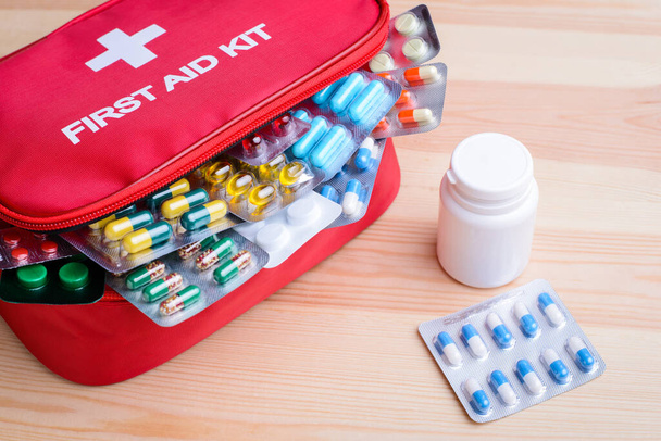 Top view on the red first aid kit box with pills in a blister pack close-up on a light wooden background with space for text and white plastic bottle of pills standing near. Medications - Fotó, kép