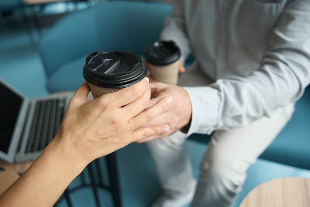 レクリエーションエリアビジネスセンターでコーヒーブレイクのための快適なソファに定住した同僚、男は女性にコーヒーを保持しています - 写真・画像