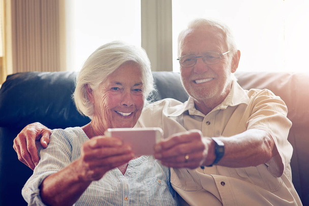 Le véritable amour non filtré. un heureux couple de personnes âgées prenant un selfie ensemble sur le canapé à la maison - Photo, image